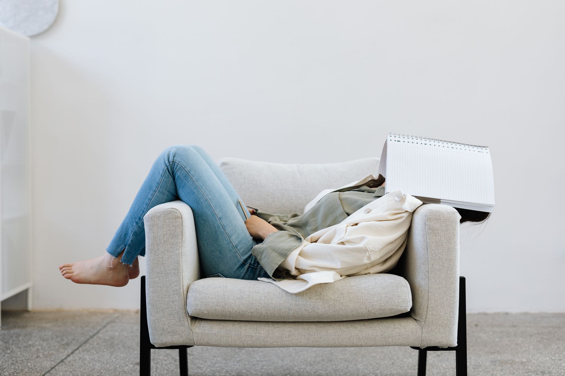 person lying on sofa chair face covered with notebook